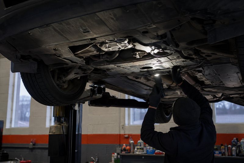 Specialist inspecting the underside of a car on a lift